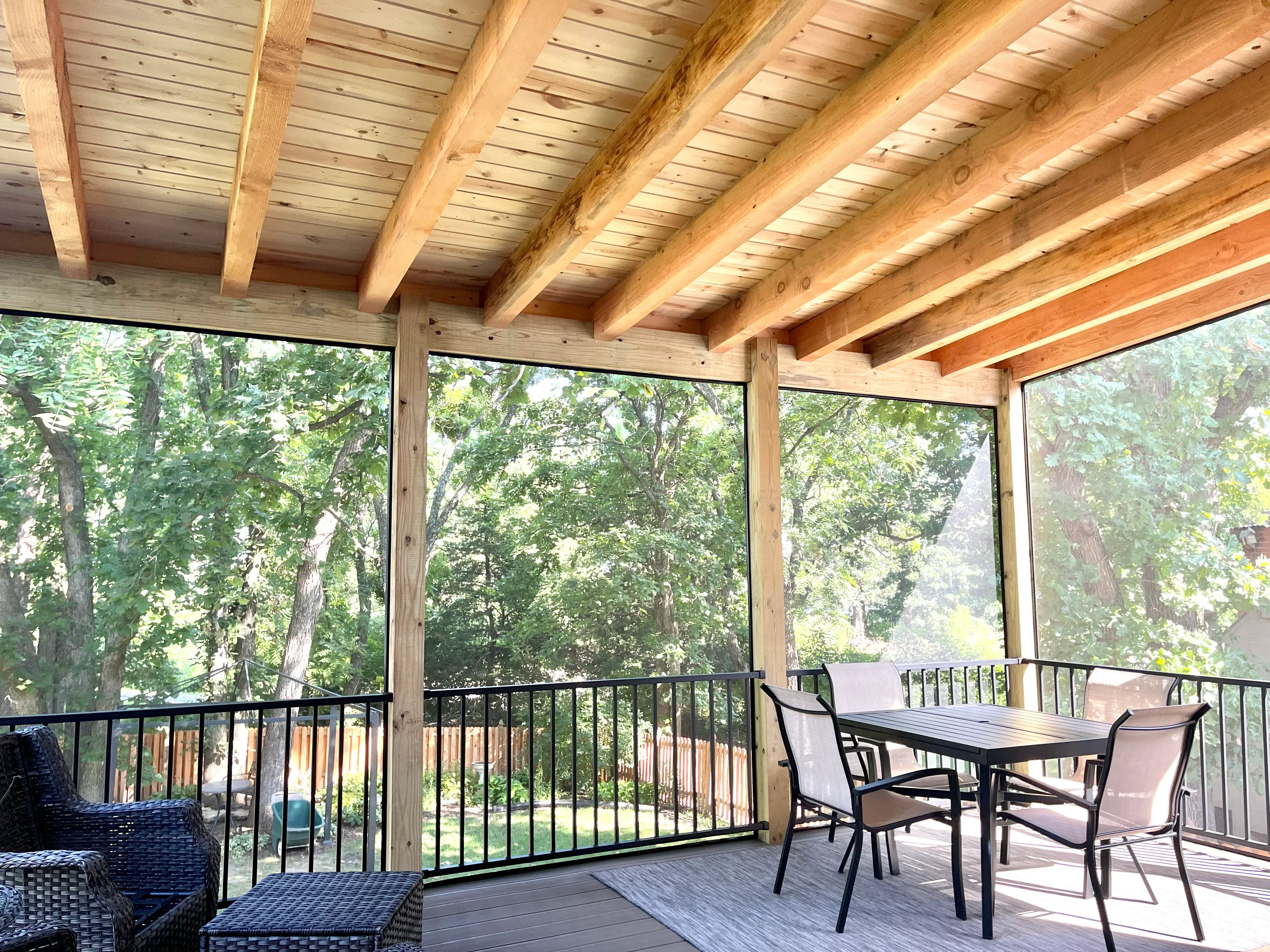 Timber frame covered deck with exposed beams, large windows, black railings, and composite decking