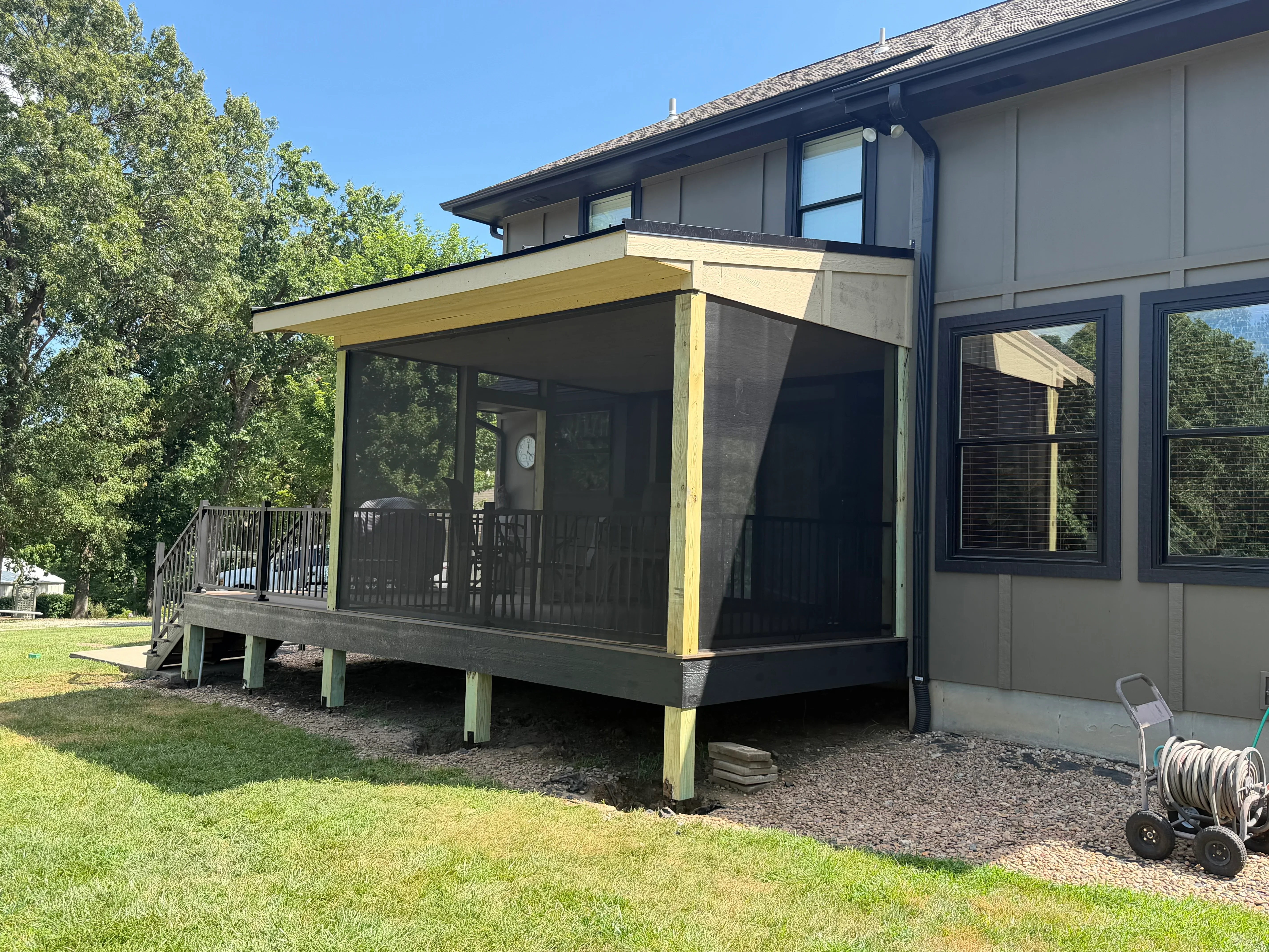 Screened porch with yellow beam framing, black screens, composite deck, and post supports
