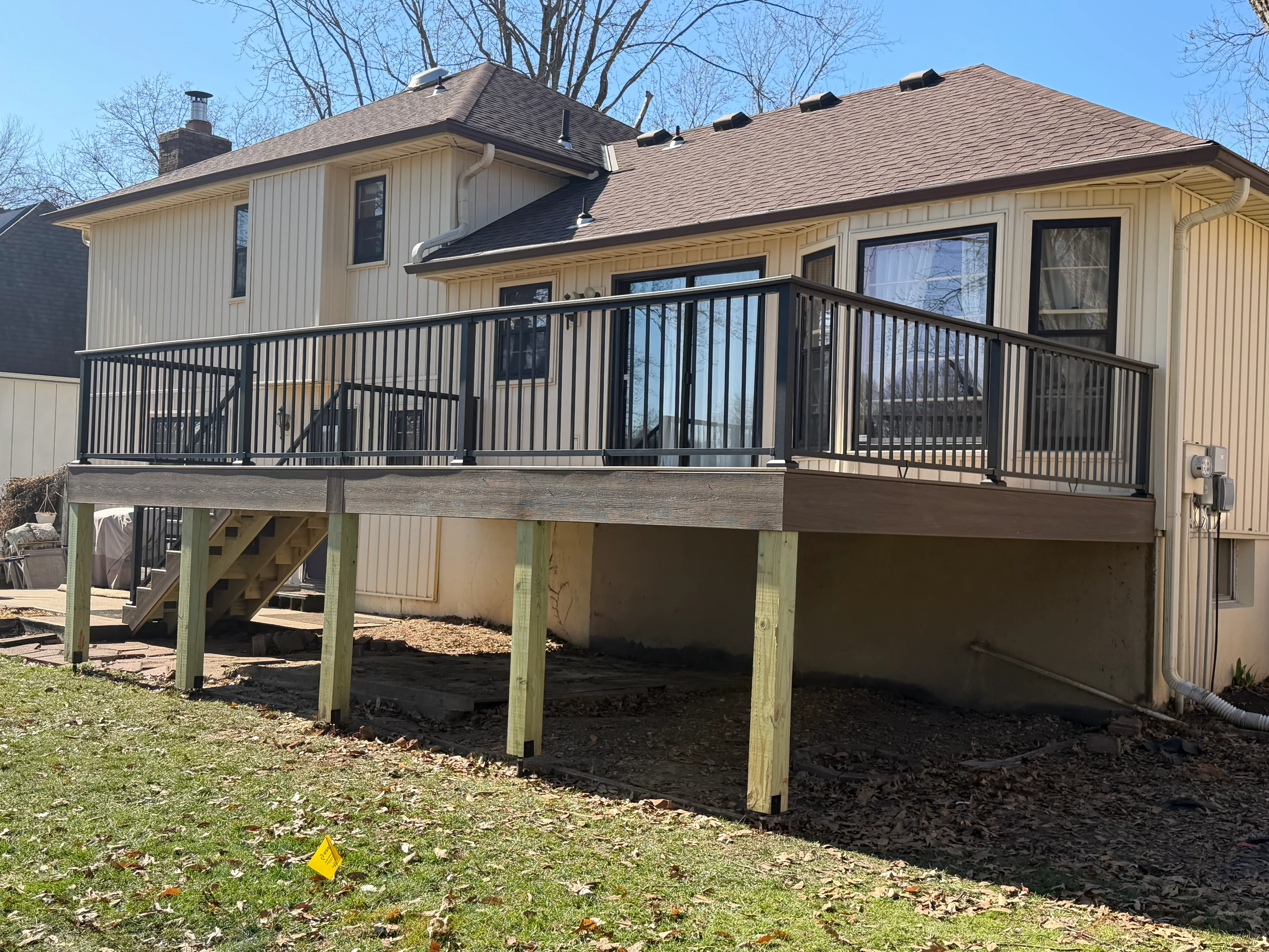 Elevated deck with black metal railing, wood posts, and composite decking on residential home