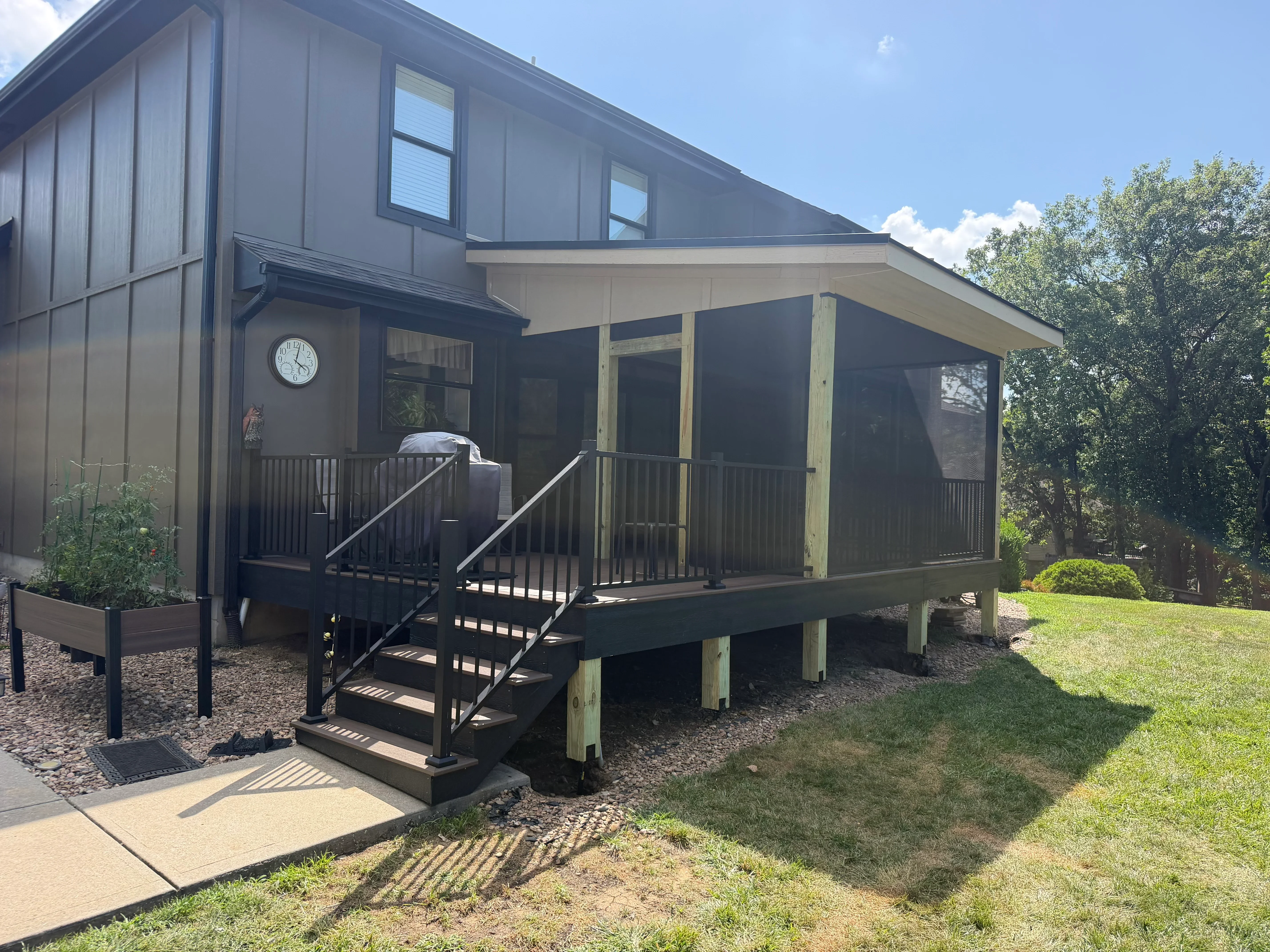 Black metal screened porch with deck, stairs, and railings on modern home with dark siding