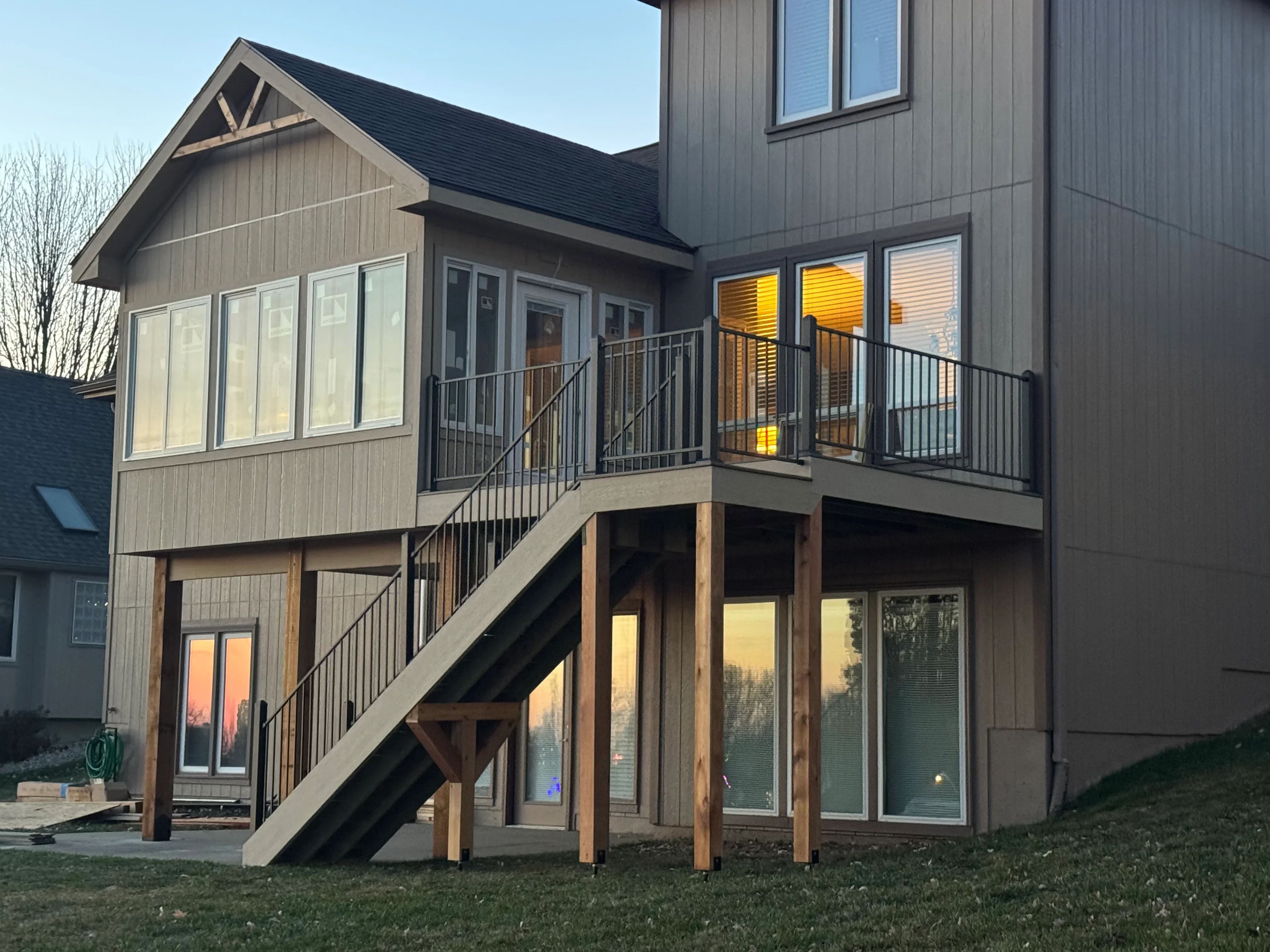 Two-story composite deck with black metal railings and wood posts attached to modern home