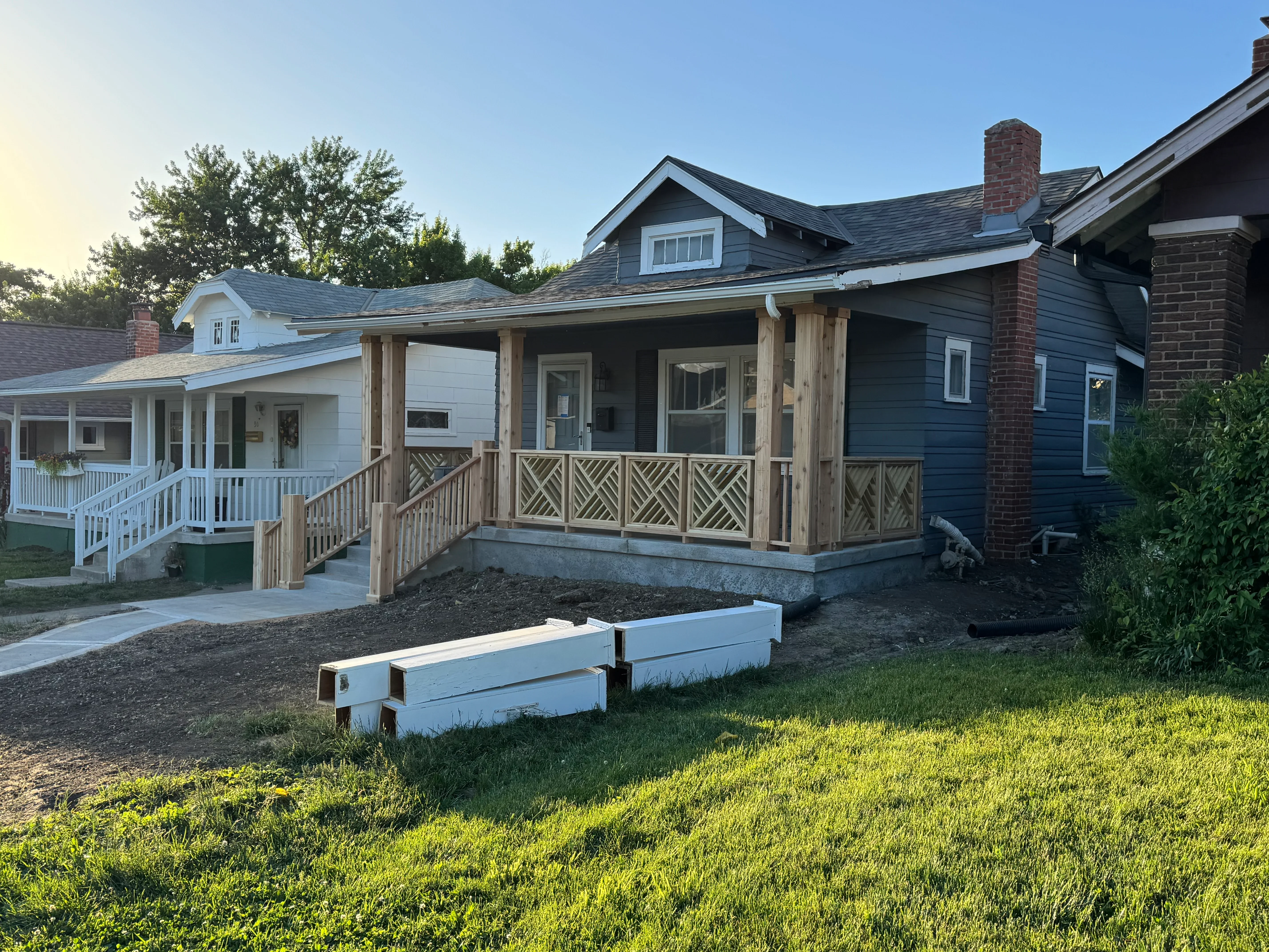 Covered porch with wood posts, beams, and geometric pattern railing on concrete foundation