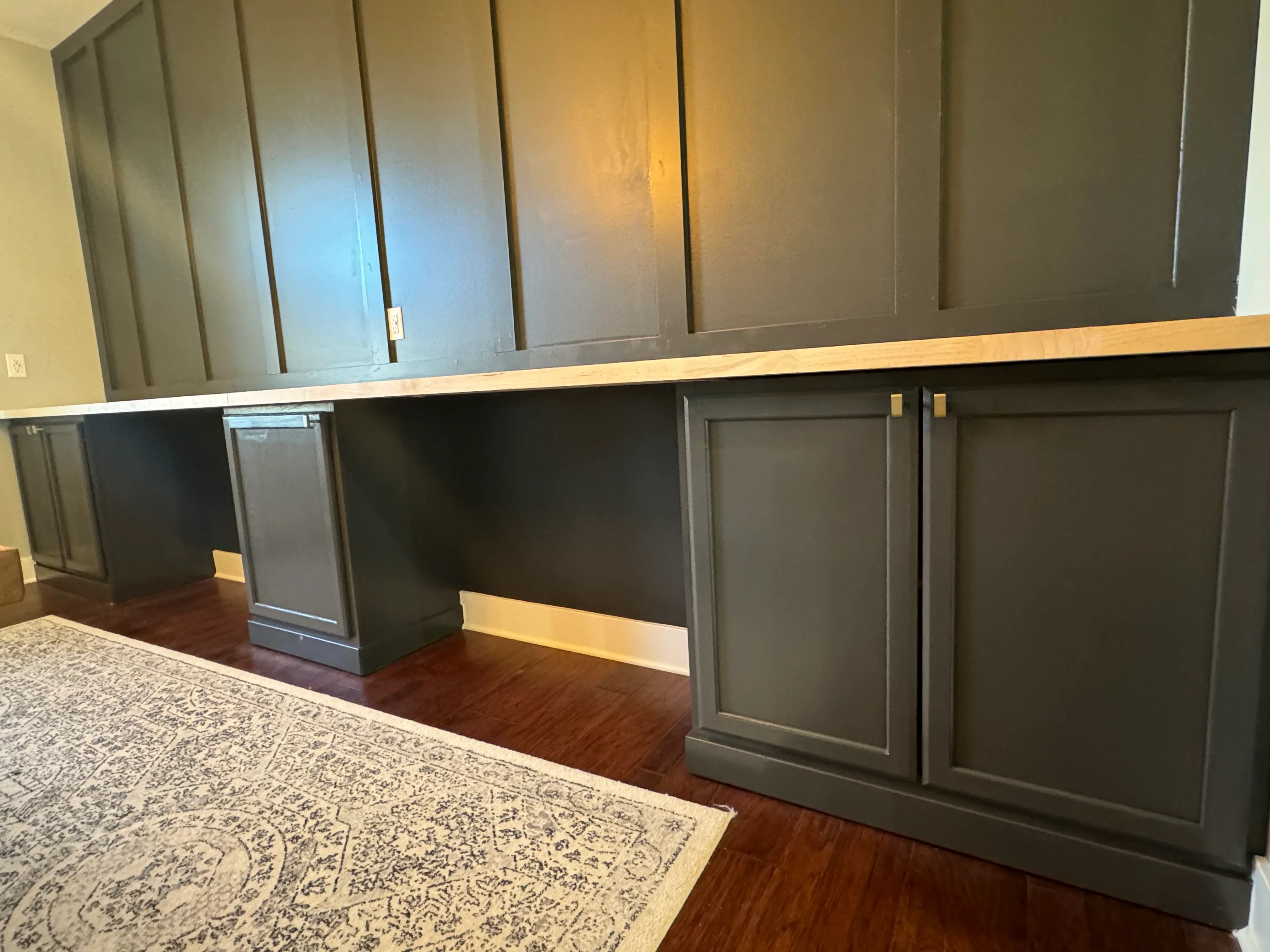 Gray painted cabinetry with recessed panels, natural wood rail trim, and wainscoting installation
