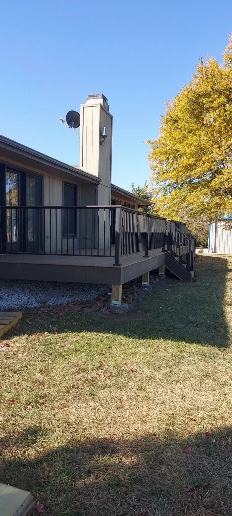 Elevated composite deck with black metal railing, stairs, and tall chimney structure on residential home