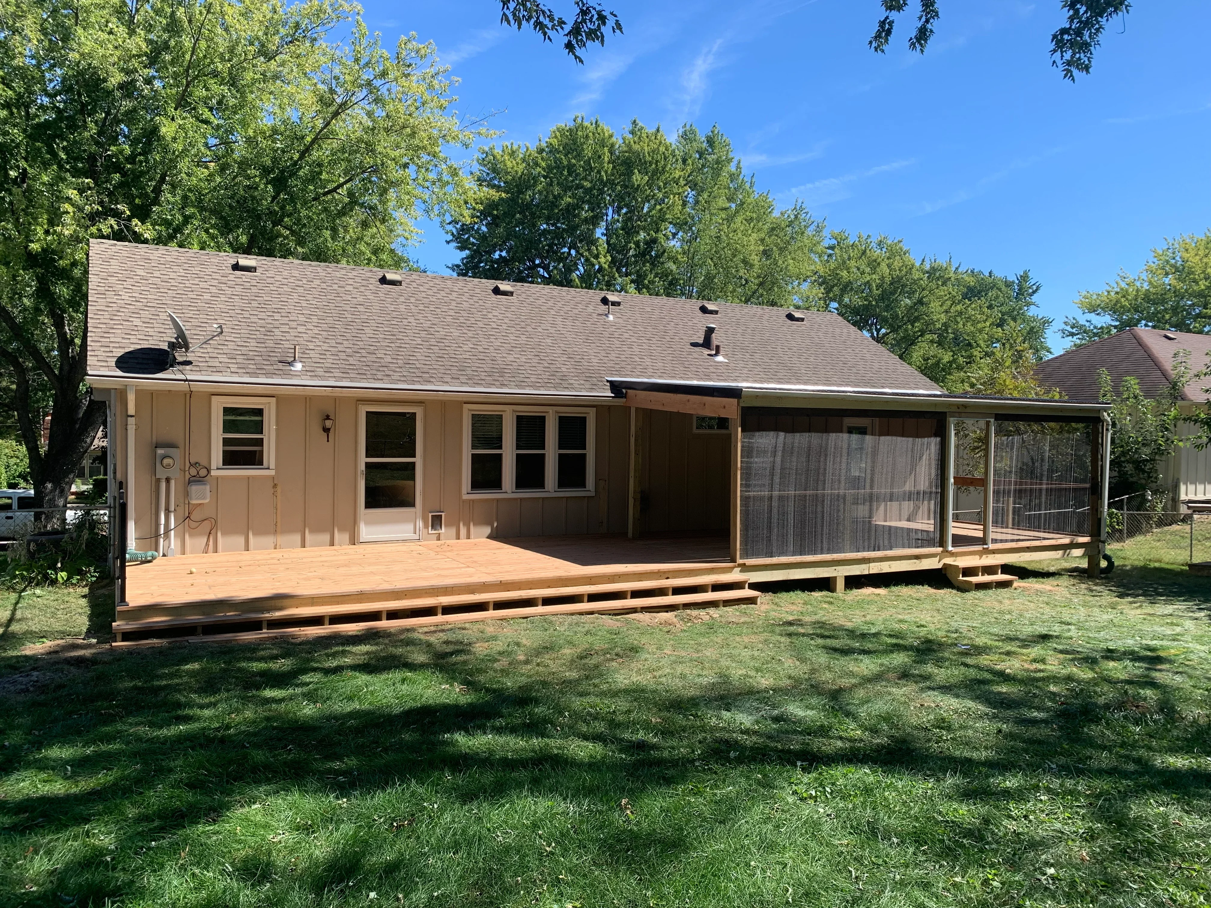 Tan house with new wood deck, covered patio, screened porch, and asphalt shingle roof