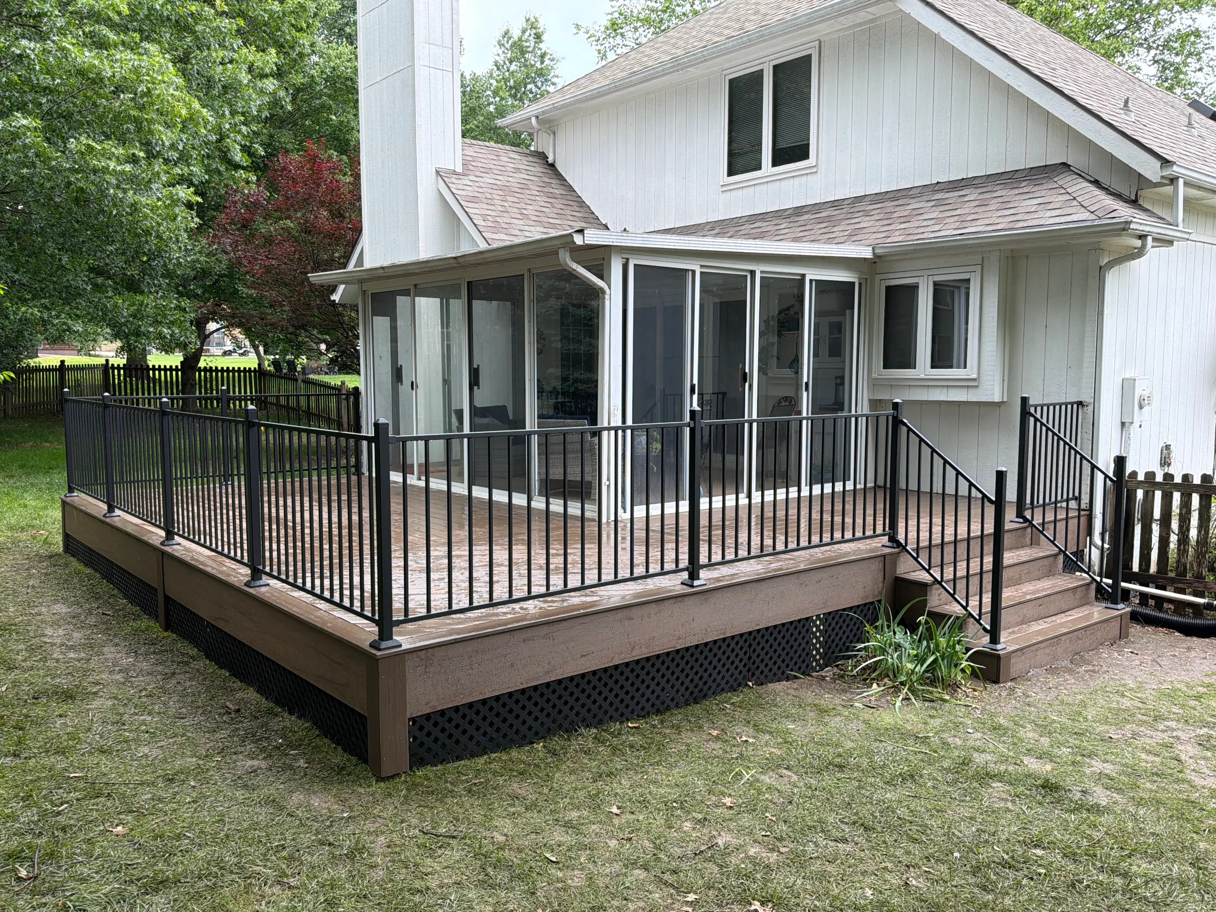 Composite deck with black aluminum railings, brown decking, and screened sunroom addition