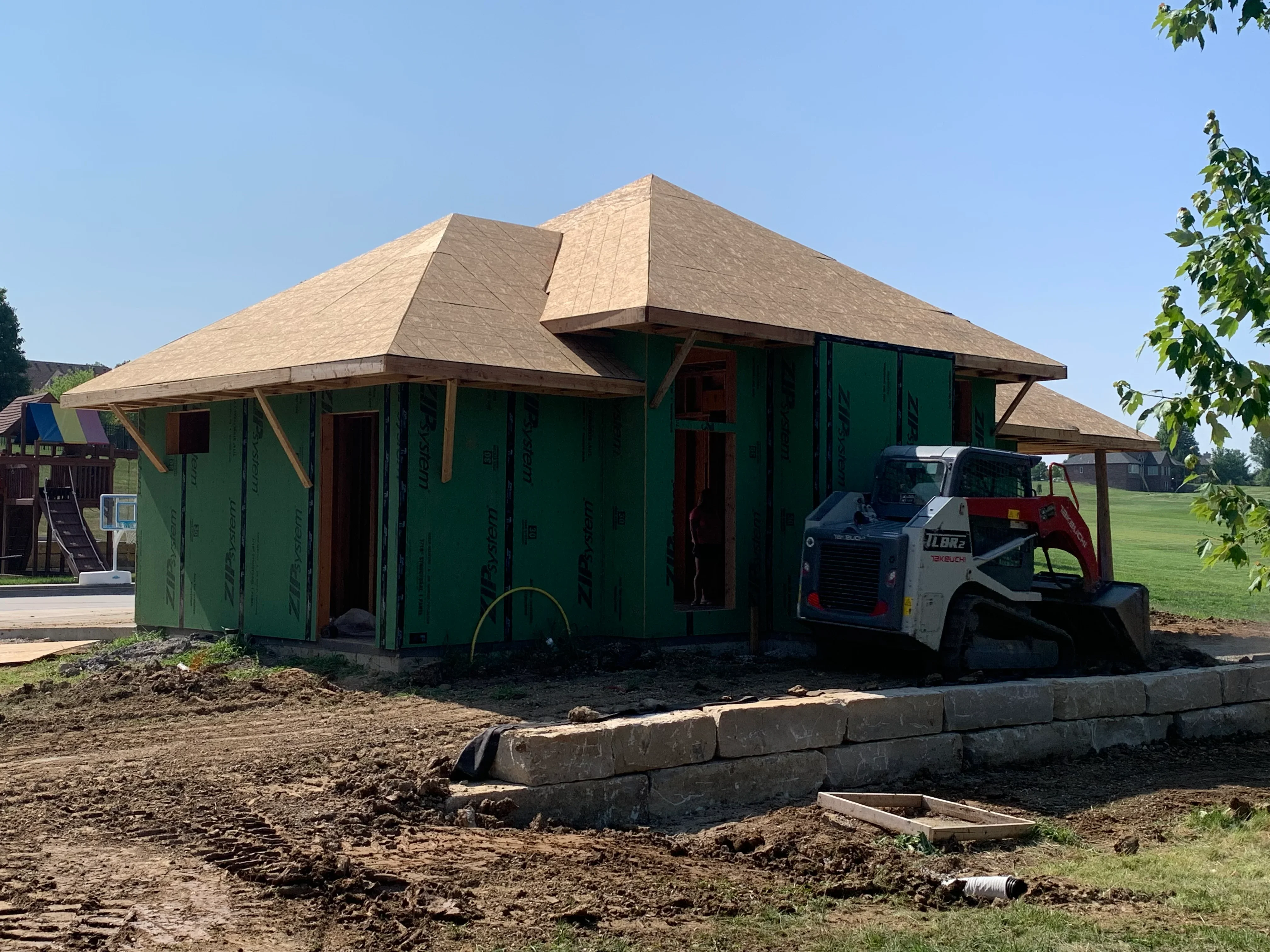New home construction with multi-pitched architectural shingle roof, timber framing, and green house wrap