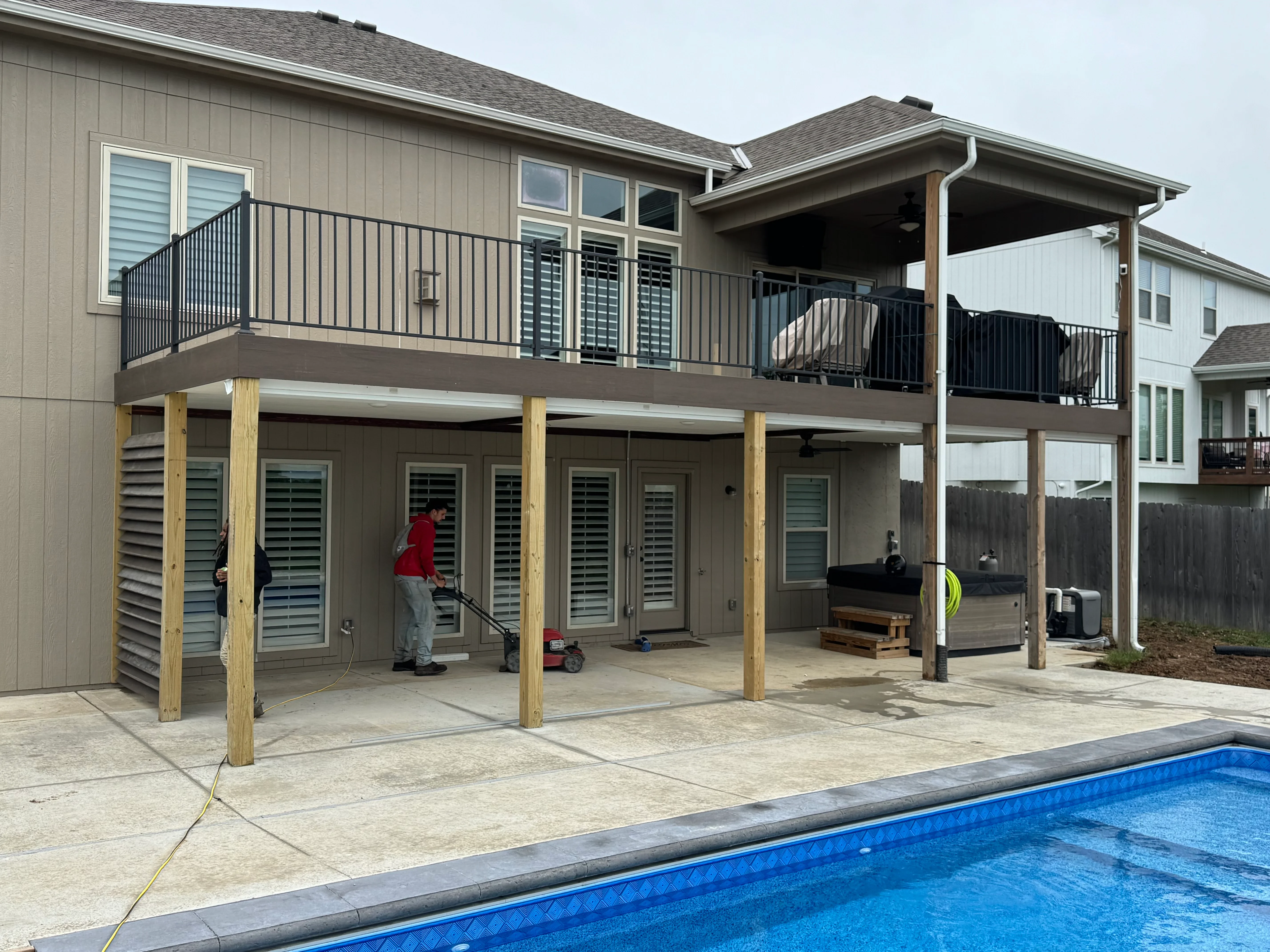 Two-story composite deck with black metal railings, timber posts, and covered patio structure by pool