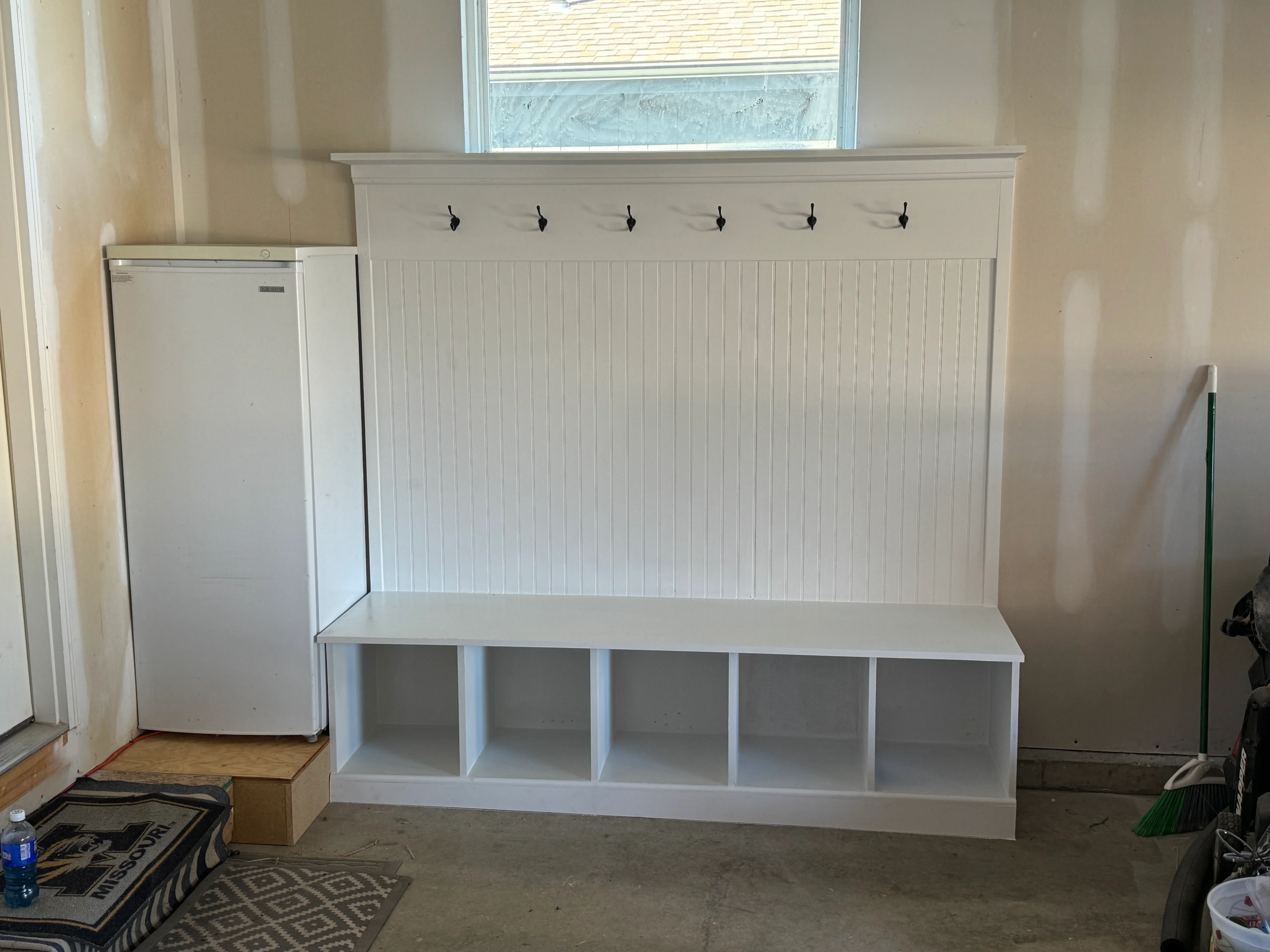 White built-in mudroom bench with five storage cubbies, shiplap wainscoting backing, and six wall-mounted hooks