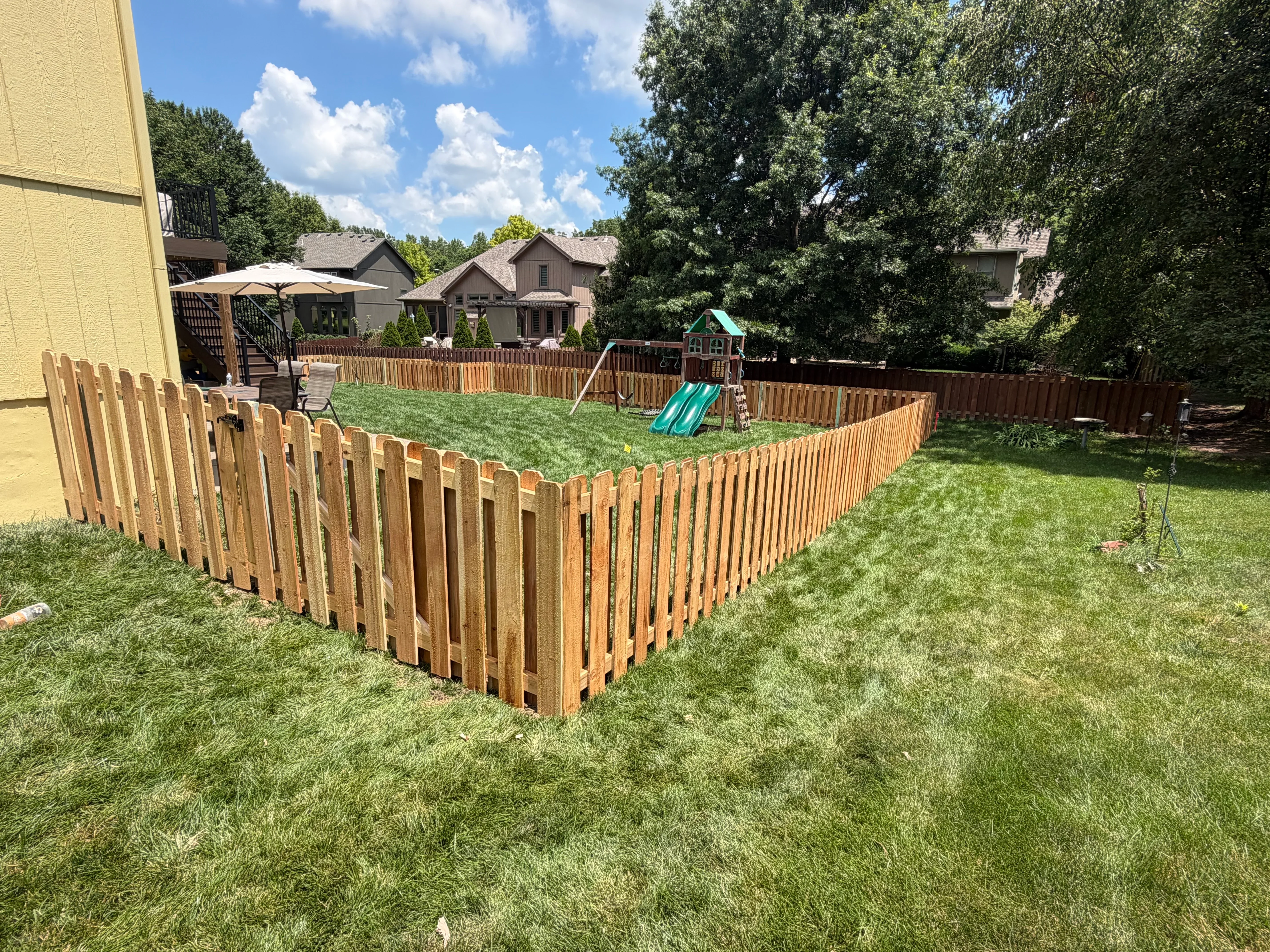 Newly installed wood picket fence surrounding backyard play area with green lawn